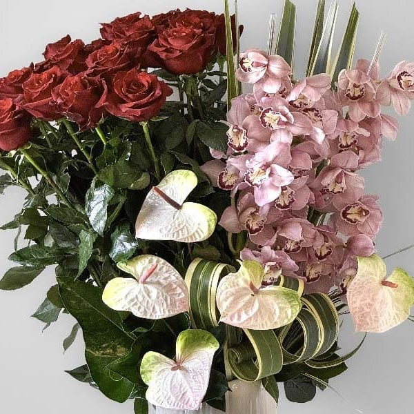 Bouquet of red roses, pink orchids, and green leaves on a light gray background