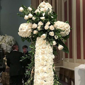 Floral cross made of white roses and greenery in a room with striped walls.