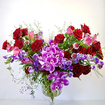 Bouquet of red, pink, and purple flowers in a clear vase on a white background