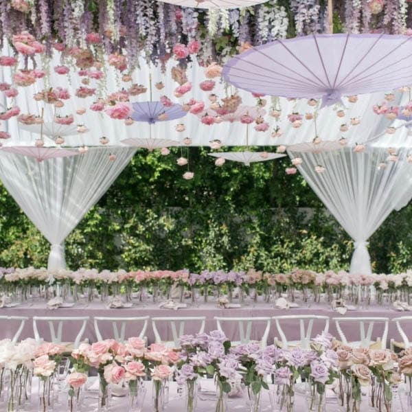 Decorative setup with floral arrangements, white parasols, and hanging flowers in a garden setting.