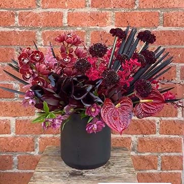 Floral arrangement in a black vase against a brick wall