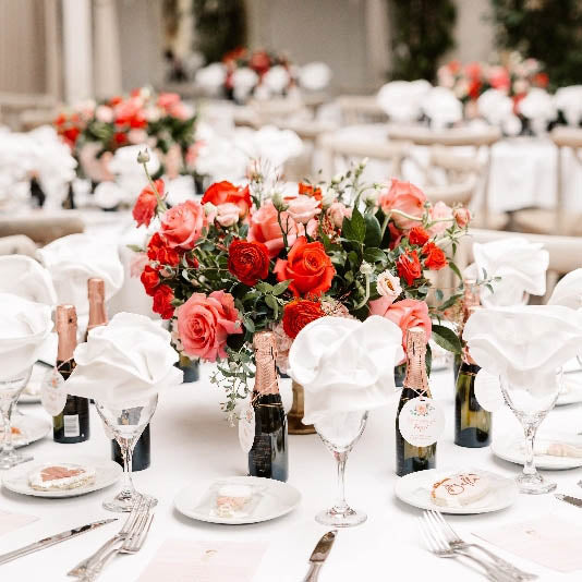 Decorated table with floral centerpieces, wine glasses, and bottles in an elegant setting.