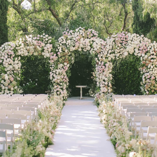 Floral archway at a wedding ceremony with chairs and a table in the background.