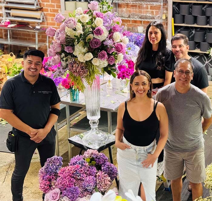 Group of people posing with floral arrangements in a workshop setting