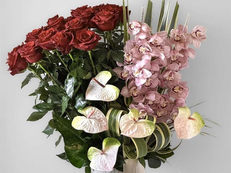 Bouquet of red roses, pink orchids, and green leaves on a light gray background