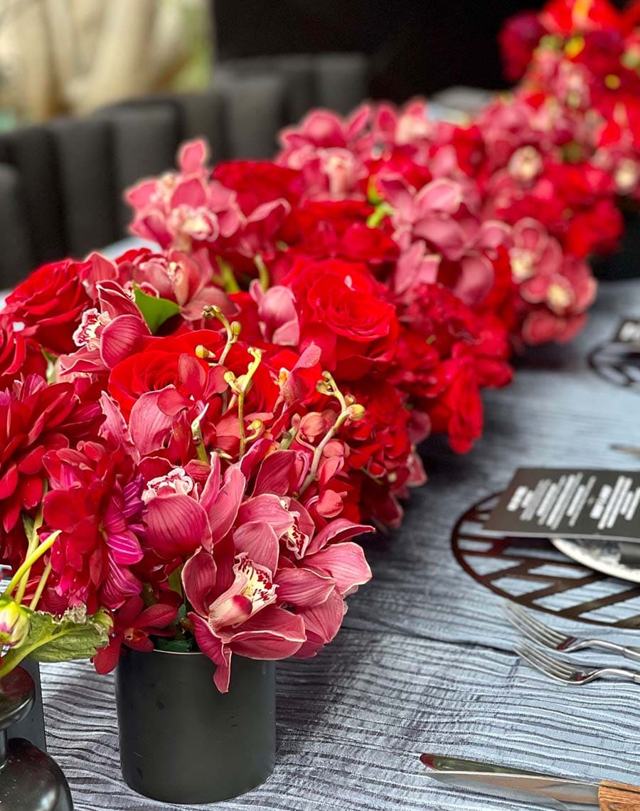 Row of red and pink flowers on a table with cutlery and a patterned napkin.