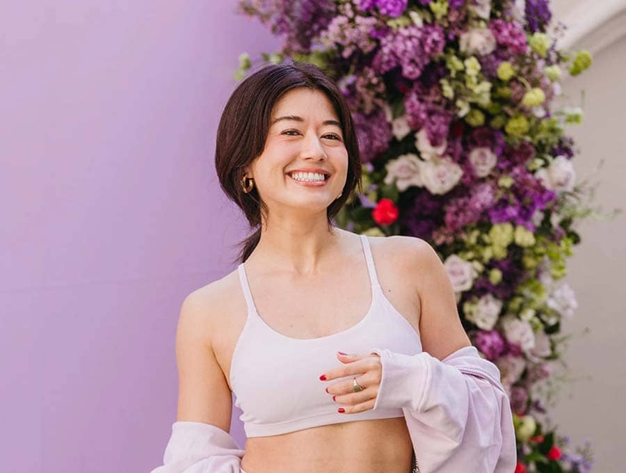 Woman in a white sports bra and leggings standing in front of a floral arrangement.