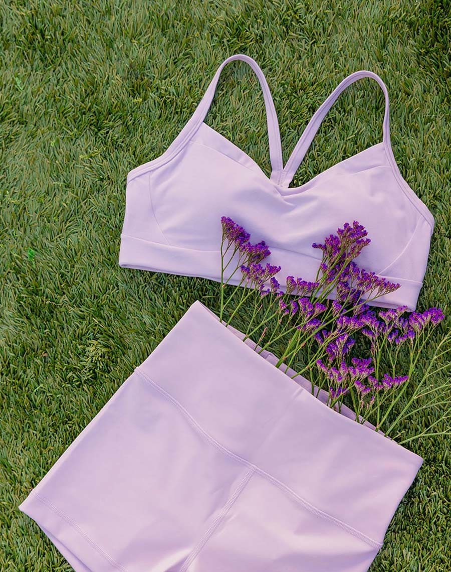 Lavender sports bra and shorts set on grass with purple flowers.