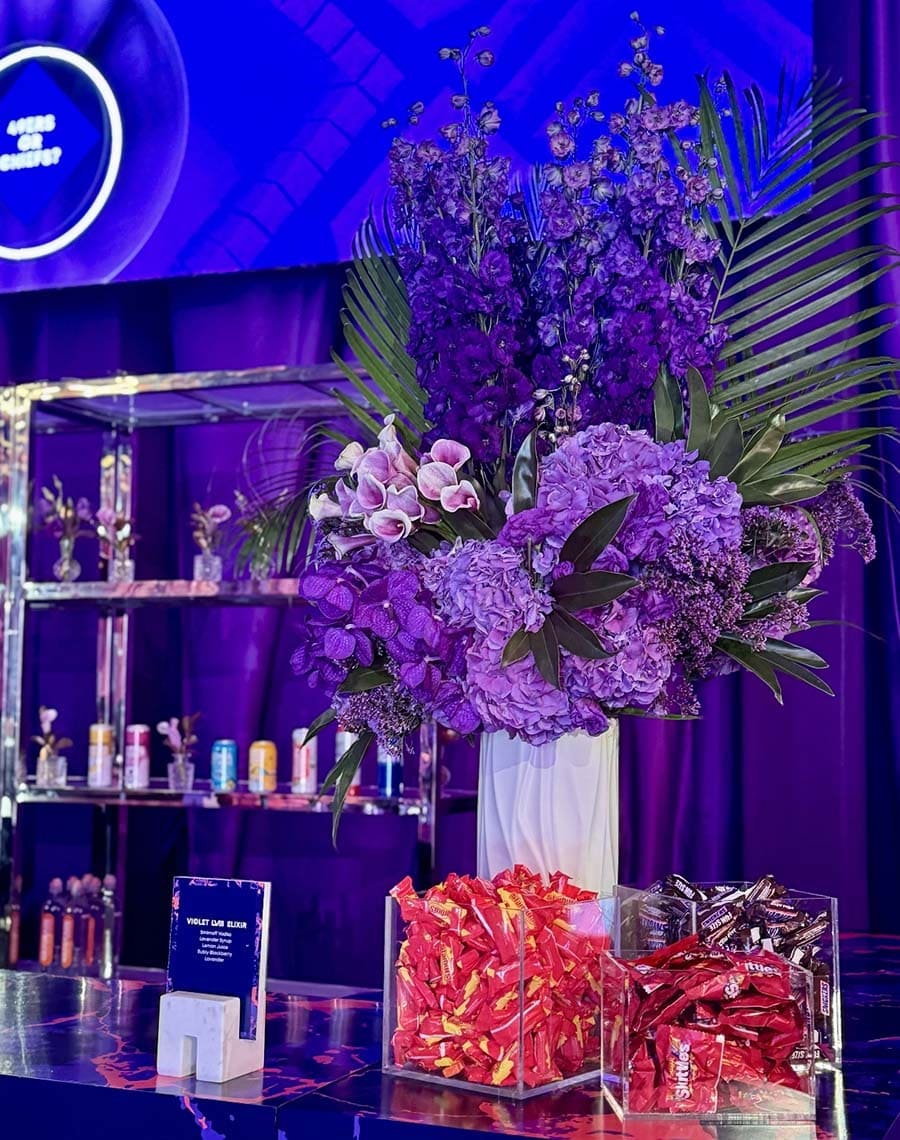 Decorative setup with purple flowers, candy, and a neon sign in the background.