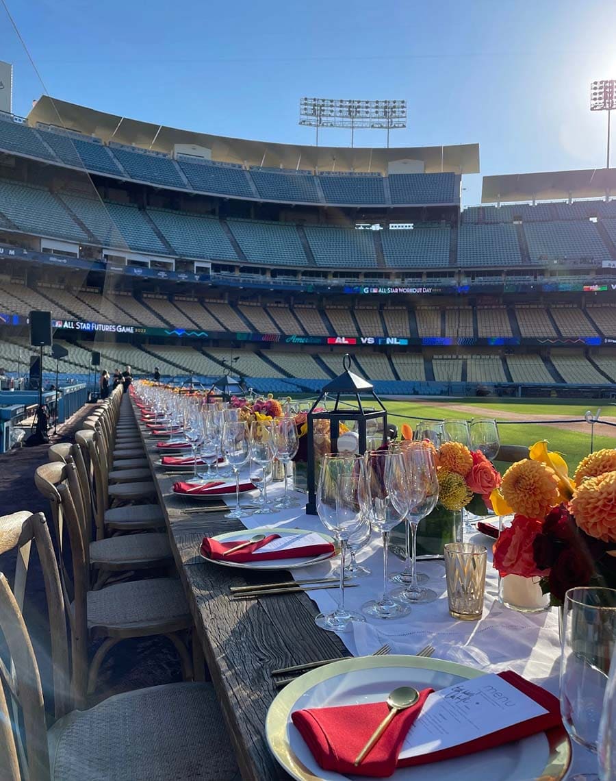 Dining setup with tables, chairs, and floral arrangements in a stadium.