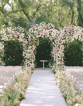 Floral archway at a wedding ceremony site with chairs and a table.
