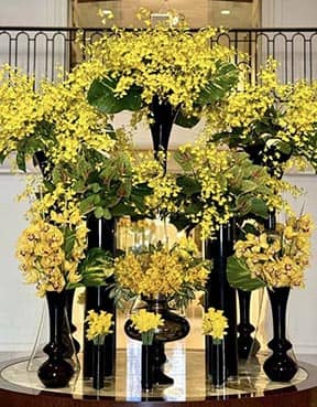 Decorative arrangement of yellow flowers in black vases on a reflective surface.