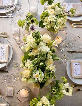 Elegant table setting with green and white floral arrangements, candles, and place cards.