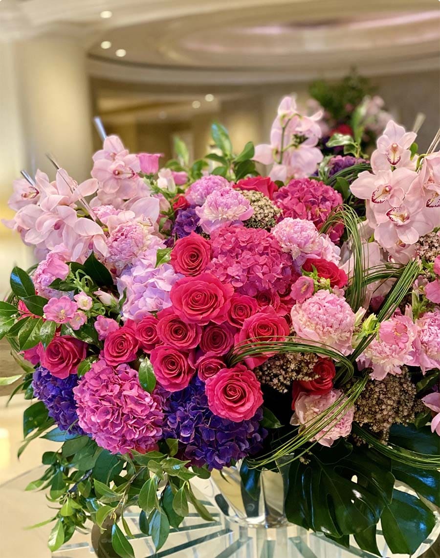 Bouquet of colorful flowers including roses and hydrangeas on a reflective surface.
