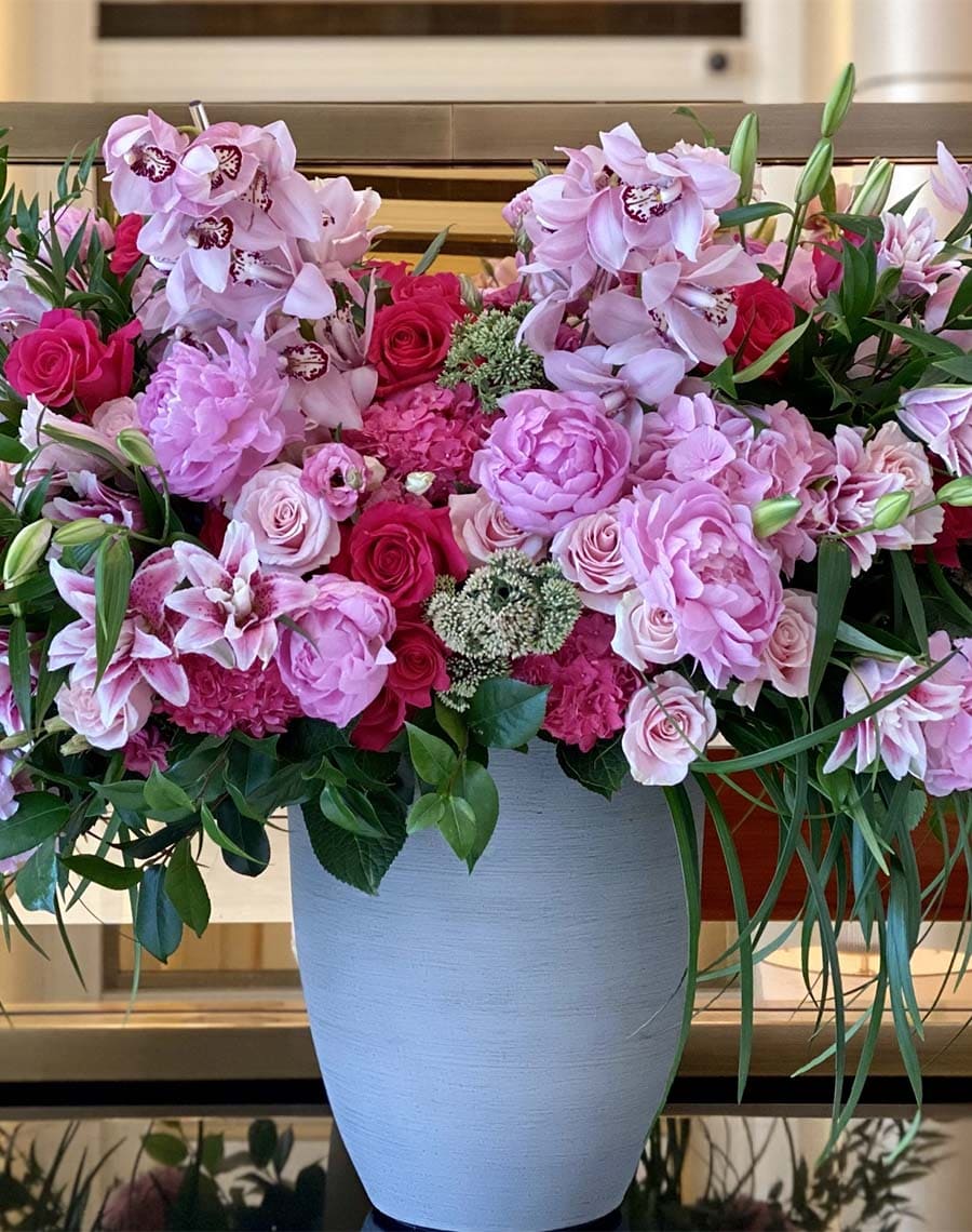 Bouquet of pink and red flowers in a white vase on a reflective surface.