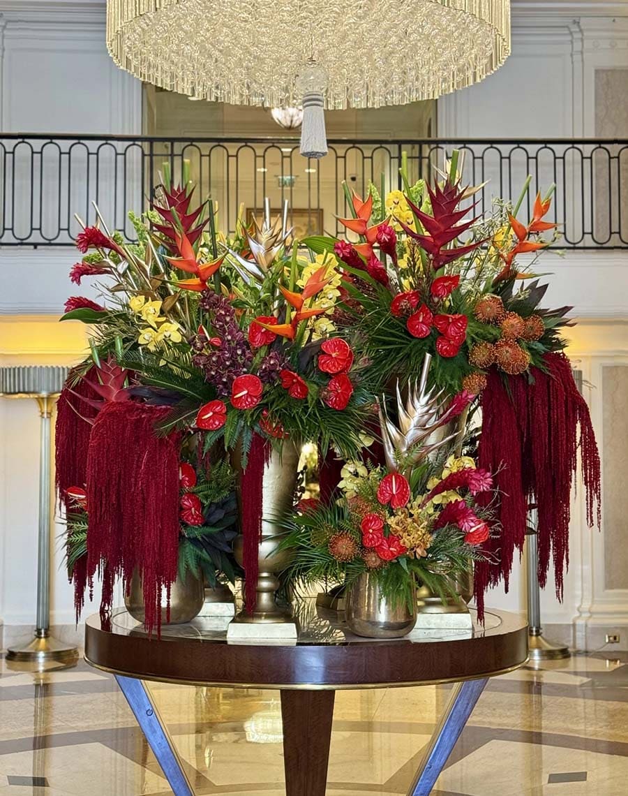 Decorative floral arrangement on a table in an elegant interior setting with a chandelier.