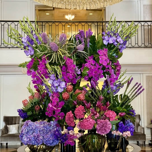 Large floral arrangement with purple, pink, and green flowers in a formal setting.