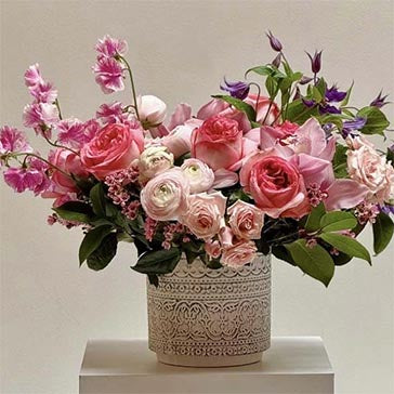 Bouquet of pink and white flowers in a decorative vase on a white surface with a light gray background
