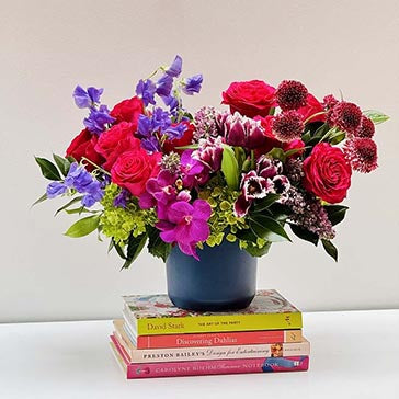 Colorful flower arrangement in a blue vase on top of books with a plain background