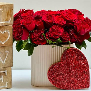 Vase of red roses with a glittery heart and wooden blocks spelling 'LOVE' on a white background