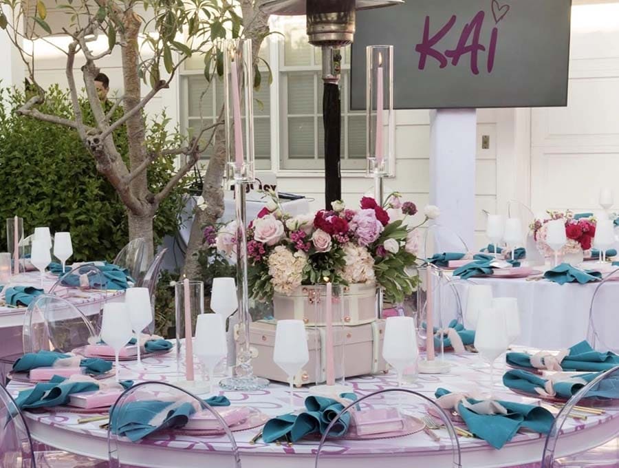 Decorated outdoor event with tables, floral arrangements, and a sign with 'KAI'.