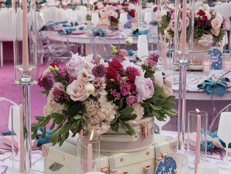 Decorative floral arrangement on a suitcase with candles and table settings in the background