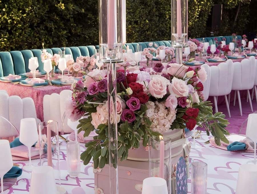 Decorative floral arrangement on a table with pink and white tablecloth, surrounded by chairs and additional tables.
