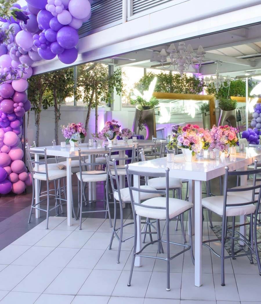 Outdoor event setup with tables, chairs, and purple balloon decorations.