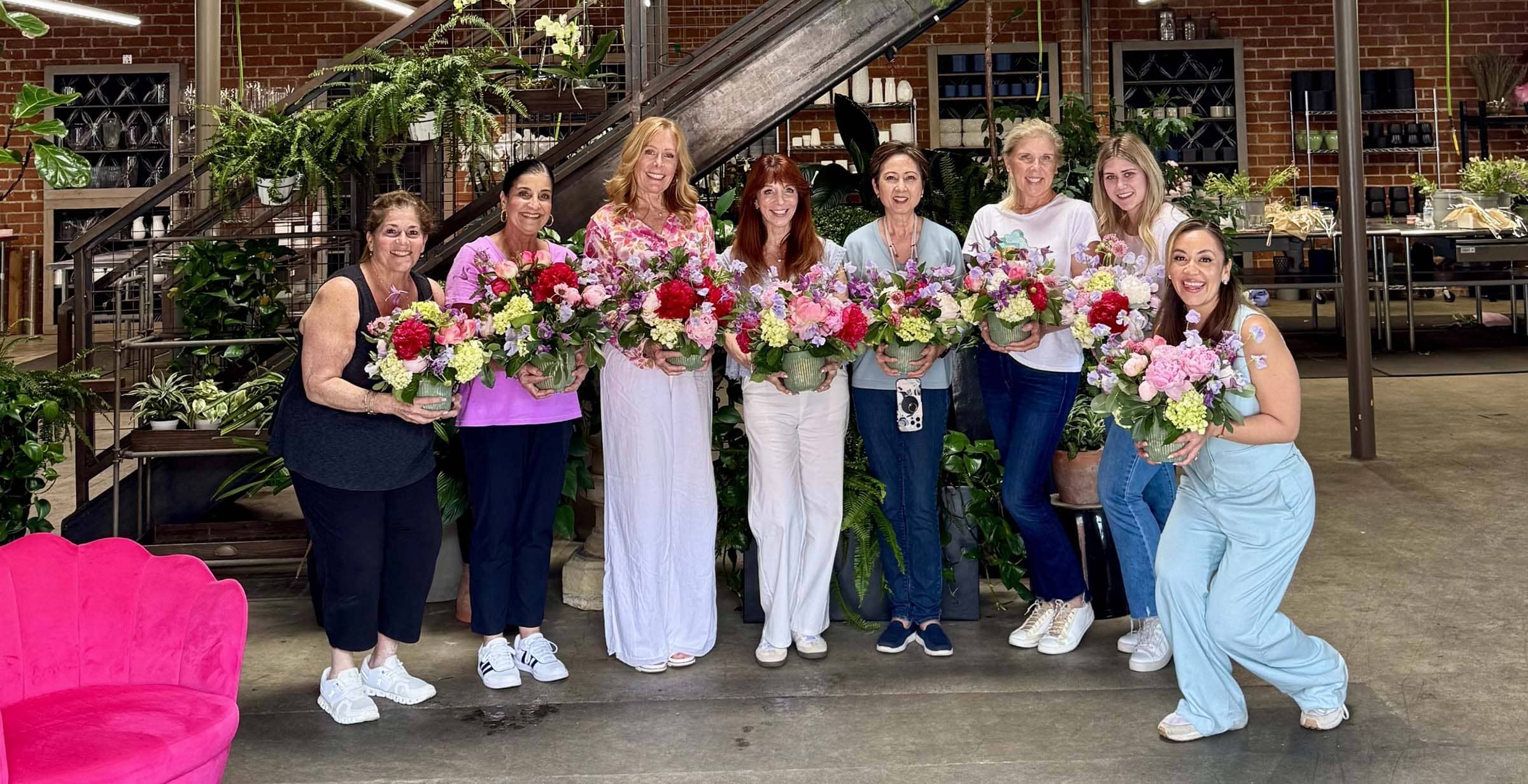Group of women holding floral arrangements in a rustic indoor setting.