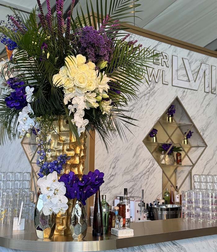 Decorative floral arrangement with purple and white flowers on a bar counter, featuring a geometric shelf in the background.
