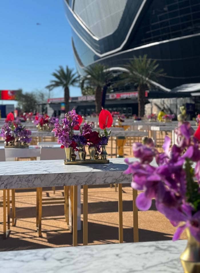 Decorative tables with flowers in front of a large building with a curved roof.
