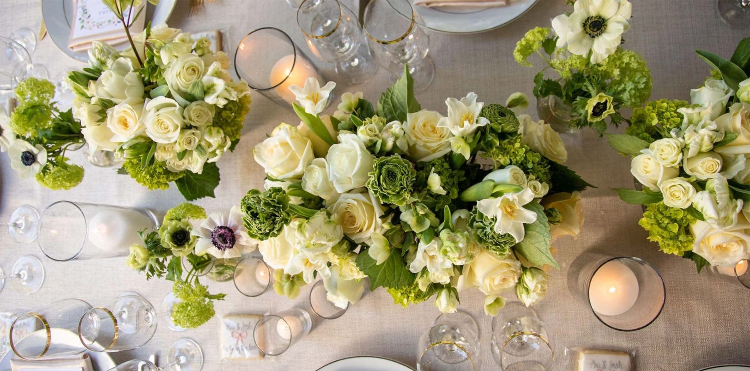 Decorative table setting with green and white floral arrangements, candles, and glassware.