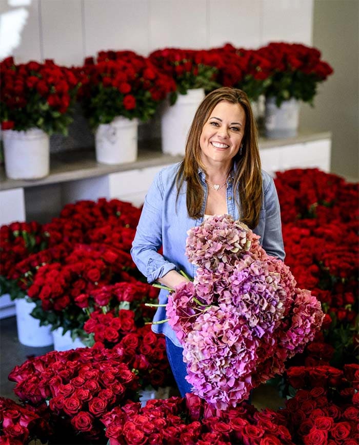 Woman holding a bouquet of pink flowers surrounded by red flowers in a warehouse setting.