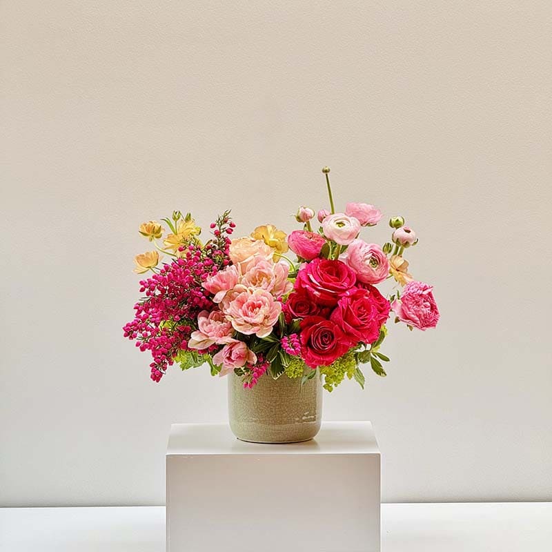 Colorful flower arrangement in a vase on a white pedestal against a light gray background