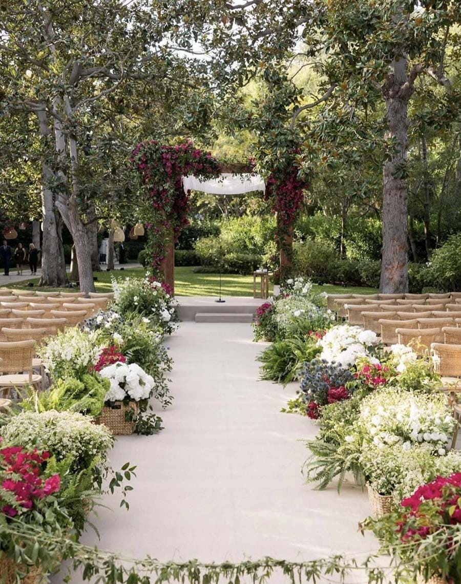 Outdoor wedding ceremony setup with floral arrangements and a canopy in a park.