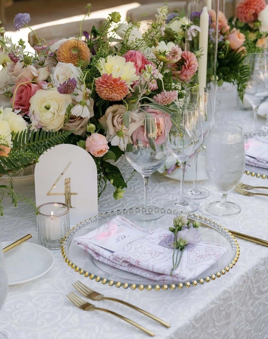 Elegant table setting with floral arrangements, candles, and gold cutlery on a white tablecloth.