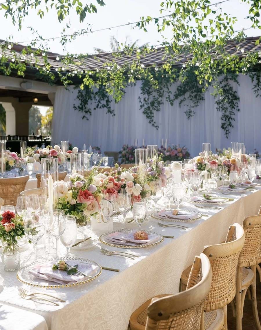 Elegant outdoor wedding reception with tables set for dinner, floral arrangements, and white tablecloths.