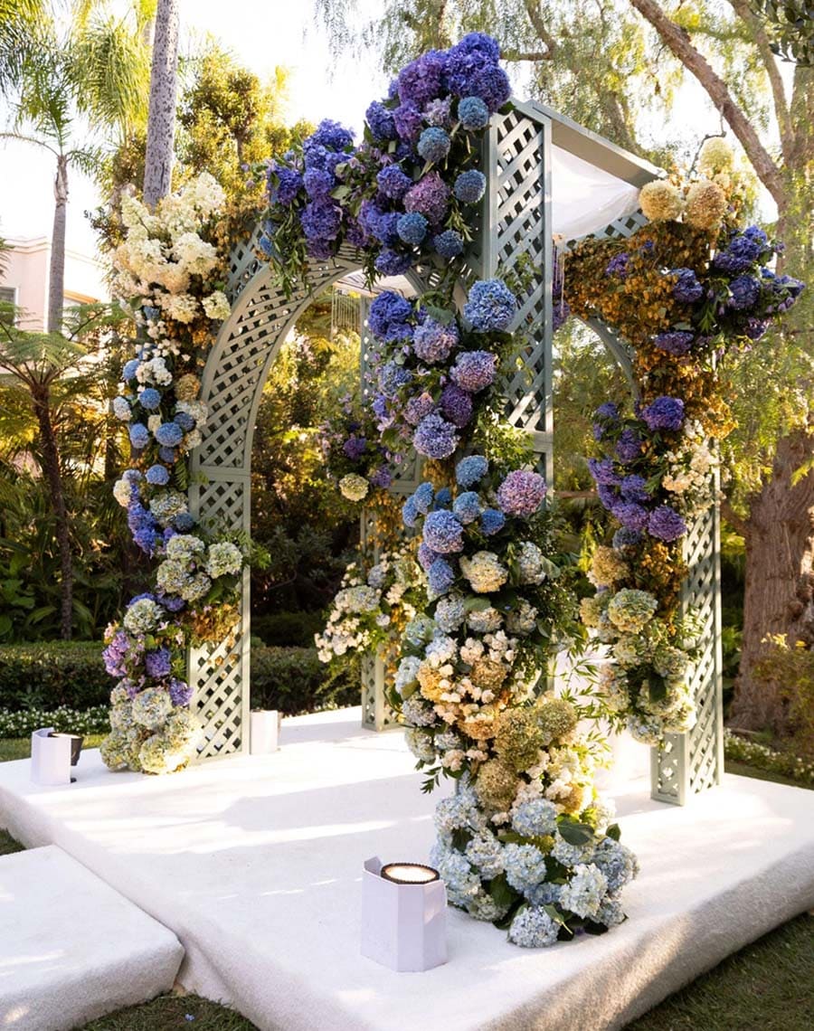 Decorative floral arch with candles on a white platform outdoors.