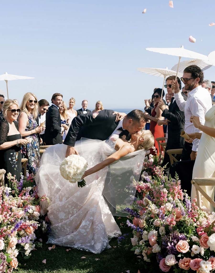 Wedding ceremony with a couple being lifted by guests, surrounded by flowers and people.