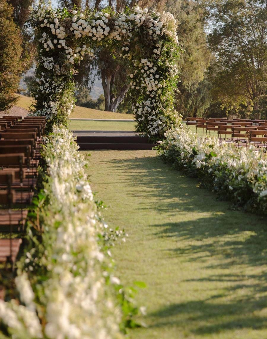 Decorative floral archway at a wedding venue with chairs on either side.