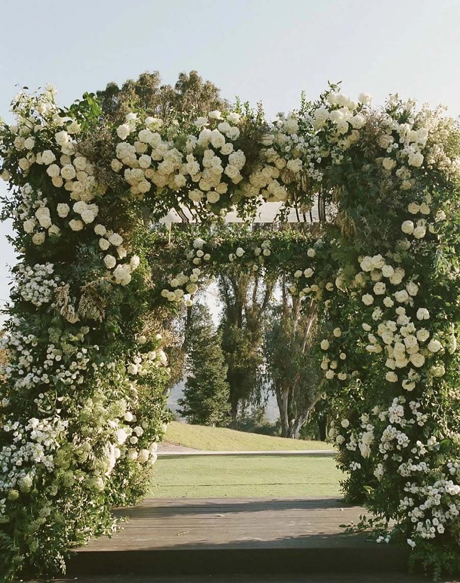 Floral archway with white flowers and greenery leading to a scenic landscape.