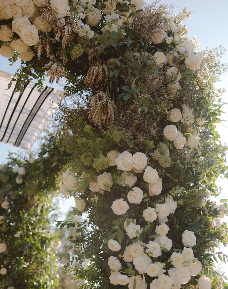 Floral archway with white flowers and greenery against a clear sky