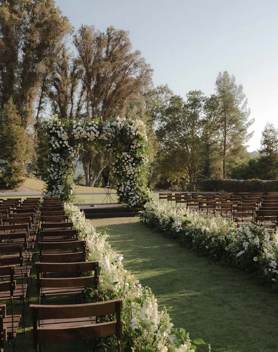 Wedding ceremony setup with floral arch and chairs on a grassy field.