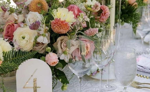 Elegant table setting with floral arrangements, candles, and gold cutlery on a white tablecloth.